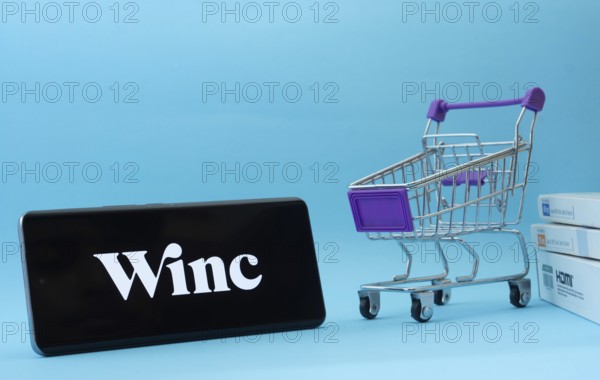 Dhaka, Bangladesh- 03 July 2025: Smartphone with Winc logo next to a small shopping cart and boxes against a blue background