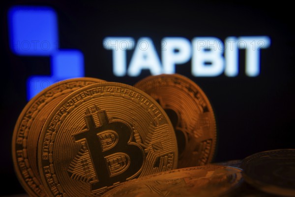 Dhaka, Bangladesh- 20 Sep 2025: Close-up of Bitcoin coins with thex Tapbit logo visible on a screen in the background