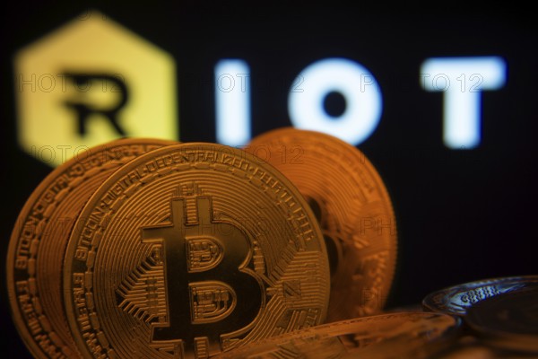 Dhaka, Bangladesh- 20 Sep 2025: Close-up of Bitcoin coins with the Riot Platforms logo visible on a screen in the background