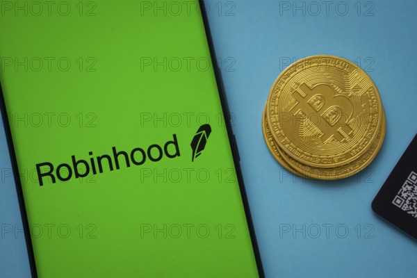Dhaka, Bangladesh- 26 Aug 2025: Robinhood logo on smartphone screen near Bitcoin coin and QR code on blue background