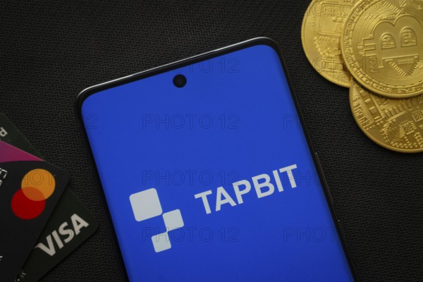 Dhaka, Bangladesh- 20 Sep 2025: Smartphone displaying Tapbit logo surrounded by Bitcoin coins and payment cards