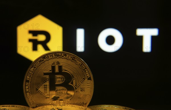 Dhaka, Bangladesh- 20 Sep 2025: Close-up of Bitcoin coins with the Riot Platforms logo visible on a screen in the background