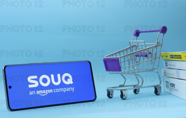 Dhaka, Bangladesh- 03 July 2025: Smartphone with Souq logo next to a small shopping cart and boxes against a blue background