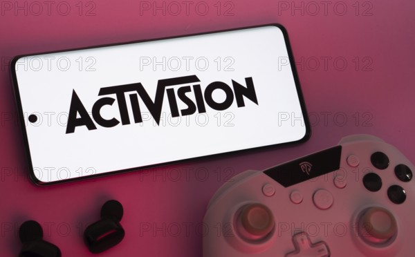 Dhaka, Bangladesh- 23 Sep 2025: Smartphone with Activision logo, game controller, and earbuds on a pink background