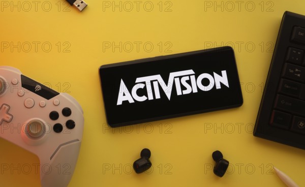 Dhaka, Bangladesh- 23 Sep 2025: Smartphone with Activision logo, game controller, and earbuds on a yellow background