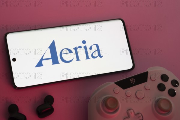 Dhaka, Bangladesh- 23 Sep 2025: Smartphone with Aeria logo, game controller, and earbuds on a pink background
