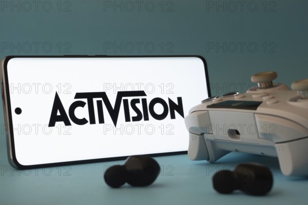 Dhaka, Bangladesh- 23 Sep 2025: A smartphone with a Activision icon next to a controller and earbuds on a blue surface