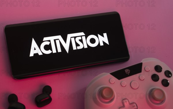 Dhaka, Bangladesh- 23 Sep 2025: Smartphone with Activision logo, game controller, and earbuds on a pink background