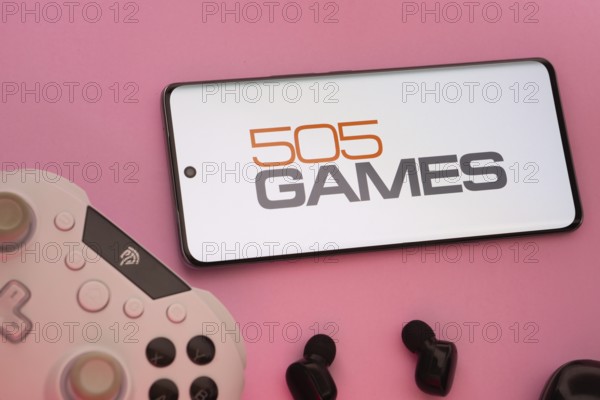 Dhaka, Bangladesh- 23 Sep 2025: Smartphone with 505 Games logo, game controller, and earbuds on a pink background