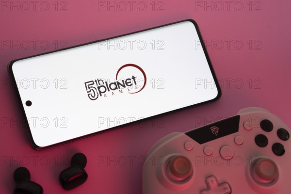 Dhaka, Bangladesh- 23 Sep 2025: Smartphone with 5th planet games logo, game controller, and earbuds on a pink background