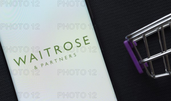 Dhaka, Bangladesh- 03 July 2025: A smartphone displaying the Waitrose & Partners logo next to a miniature shopping cart on a background