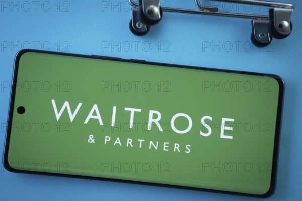 Dhaka, Bangladesh- 03 July 2025: Smartphone screen showing the Waitrose & Partners logo with shopping cart wheels on a blue background