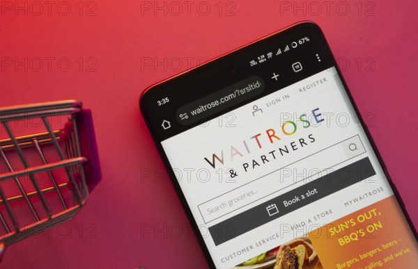 Dhaka, Bangladesh- 23 June 2025: A smartphone displaying the Waitrose & Partners website with a shopping cart is shown on a vibrant background