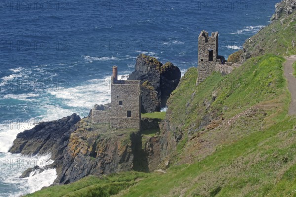 Historic ruins perched on a cliff, surrounded by rocky coastline and surging sea waves, engine room of an old copper mine, Cornwall, Great Britain