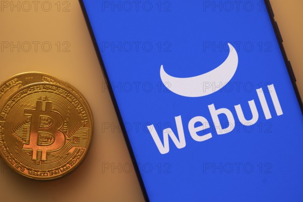 Bitcoin coin next to a smartphone showing Webull logo on a blue background