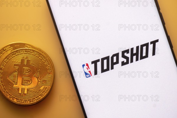 Bitcoin coin near smartphone with TopShot and NBA logos on a white screen