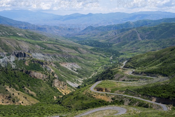 Winding roads lead down through a green valley into mountainous terrain under a clear sky, view from Vardenyats Pass or Selim Pass, Vayots Dzor Province, Armenia