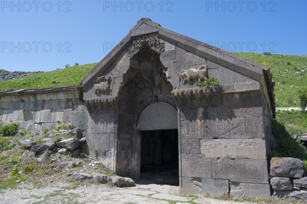 An old stone building with reliefs and a large entrance surrounded by green hills, Selim Caravanserai, Orbelian Caravanserai, Vayots Dzor Province, Armenia