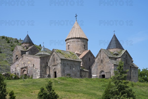An old monastery with several towers and cross-decorated roofs on a green hill under a clear blue sky, Goshavank Monastery, Tavush Province, Armenia