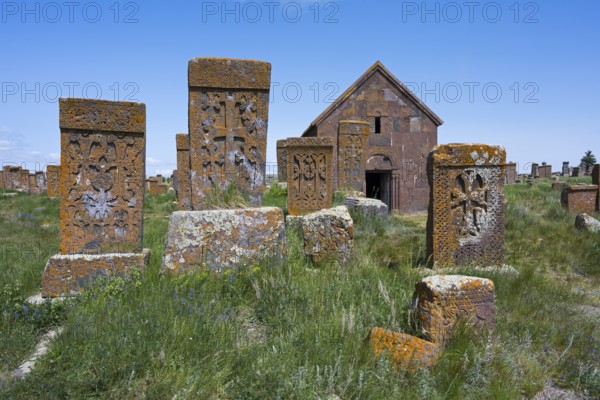 Old gravestones and a chapel in a green cemetery under a bright blue sky, cross stones, the world's largest field of Khachkars, Noratus cemetery, Noradus, Gegharkunik province, Armenia