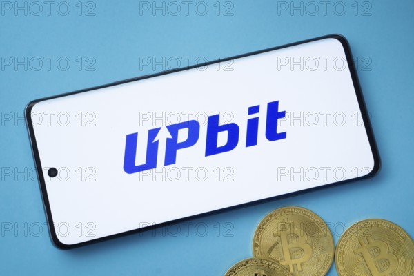 Dhaka, Bangladesh- 19 Sep 2025: Upbit logo on smartphone screen near Bitcoin coin and QR code on blue background