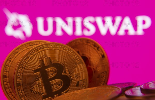 Dhaka, Bangladesh- 09 Sep 2025: Close-up of Bitcoin coins with the Uniswap logo visible on a screen in the background