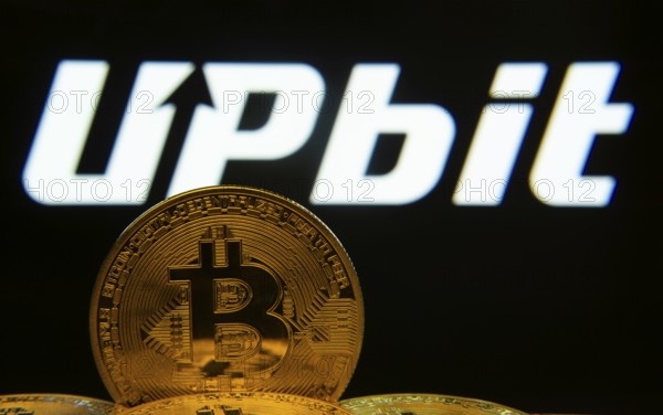 Dhaka, Bangladesh- 18 Sep 2025: Close-up of Bitcoin coins with thex Upbit logo visible on a screen in the background