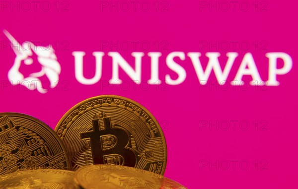 Dhaka, Bangladesh- 09 Sep 2025: Close-up of Bitcoin coins with the Uniswap logo visible on a screen in the background