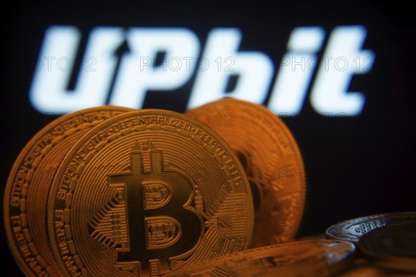 Dhaka, Bangladesh- 18 Sep 2025: Close-up of Bitcoin coins with thex Upbit logo visible on a screen in the background