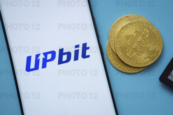 Dhaka, Bangladesh- 26 Aug 2025: Upbit logo on smartphone screen near Bitcoin coin and QR code on blue background