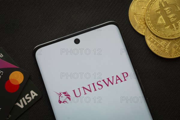 Dhaka, Bangladesh- 19 Sep 2025: Smartphone displaying Uniswap logo surrounded by Bitcoin coins and payment cards