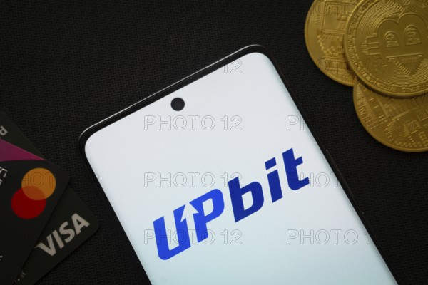 Dhaka, Bangladesh- 19 Sep 2025: Smartphone displaying Upbit logo surrounded by Bitcoin coins and payment cards