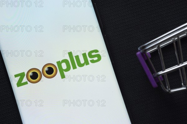 Dhaka, Bangladesh- 03 July 2025: A smartphone displaying the zooplus logo next to a miniature shopping cart on a background
