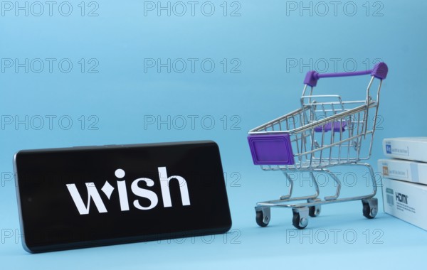 Dhaka, Bangladesh- 03 July 2025: Smartphone with Wish logo next to a small shopping cart and boxes against a blue background