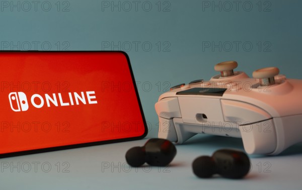 Dhaka, Bangladesh- 15 July 2025: A smartphone with a nintendo online icon next to a controller and earbuds on a blue surface