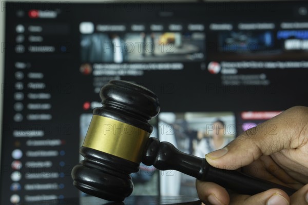 Dhaka, Bangladesh- 20 June 2025: A hand holds a gavel in front of a computer screen displaying youtube website