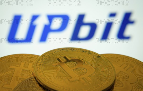Dhaka, Bangladesh- 18 Sep 2025: Close-up of Bitcoin coins with thex Upbit logo visible on a screen in the background
