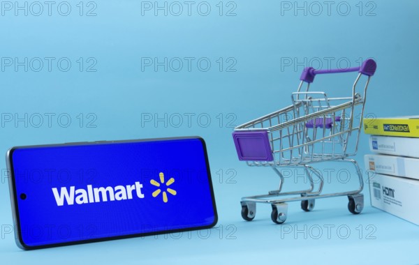 Dhaka, Bangladesh- 03 July 2025: Smartphone with Walmart logo next to a small shopping cart and boxes against a blue background