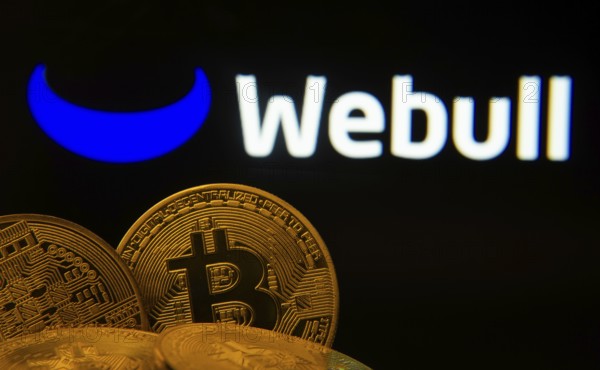 Dhaka, Bangladesh- 04 April 2025: Close-up of Bitcoin coins with the webull logo visible on a screen in the background