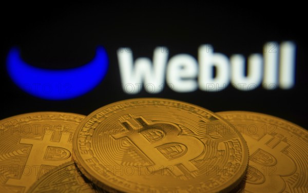 Dhaka, Bangladesh- 27 July 2025: Close-up of Bitcoin coins with the webull logo visible on a screen in the background