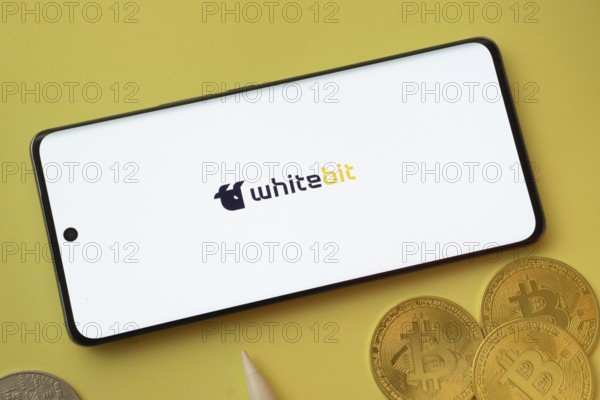 Dhaka, Bangladesh- 03 June 2025: whitebit logo on smartphone screen near Bitcoin coin and QR code on blue background