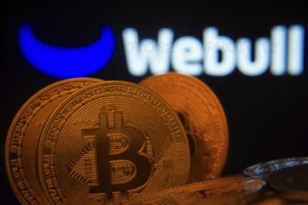 Dhaka, Bangladesh- 03 Sep 2025: Close-up of Bitcoin coins with the webull logo visible on a screen in the background