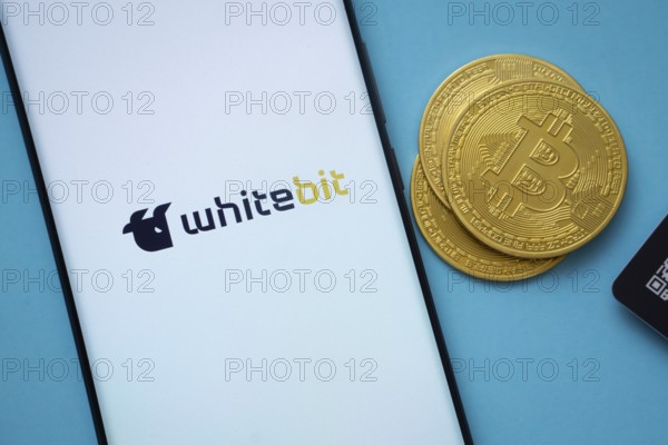 Dhaka, Bangladesh- 03 Sep 2025: Whitebit logo on smartphone screen near Bitcoin coin and QR code on blue background