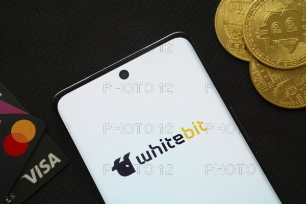 Dhaka, Bangladesh- 15 June 2025: Smartphone displaying whitebit logo surrounded by Bitcoin coins and payment cards
