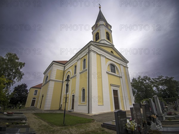 Yellow church at a cemetery with gravestones under a cloudy sky, Kammersdorf Hollabrunn Weinviertel Lower Austria Austria