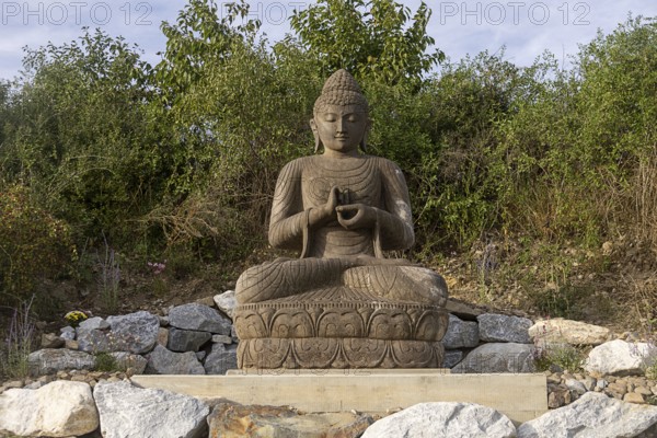 Sitting Buddha statue surrounded by stones and vegetation, Stupa am Wagram Grafenwörth Weinviertel Lower Austria Austria