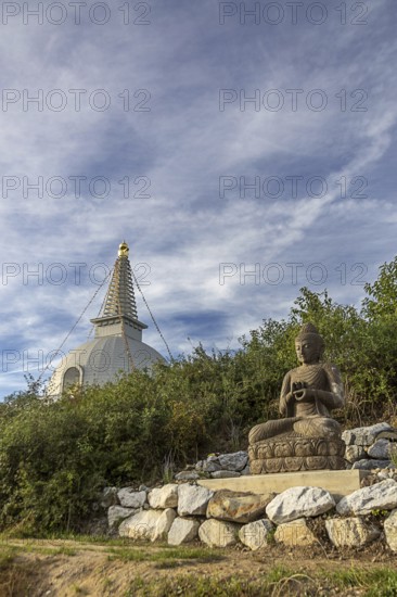 Buddha statue sitting on stones with a pagoda in the background and cloudy sky, Stupa am Wagram Grafenwörth Weinviertel Lower Austria Austria