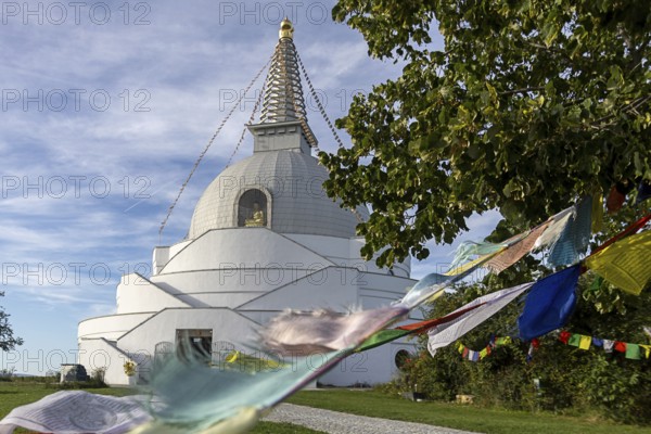 White stupa with colourful prayer flags, peaceful surroundings, green foliage, blue sky, Stupa am Wagram Grafenwörth Weinviertel Lower Austria Austria