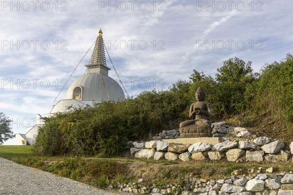 Buddha statue sitting on stones next to a pagoda in a green landscape, Stupa am Wagram Grafenwörth Weinviertel Lower Austria Austria