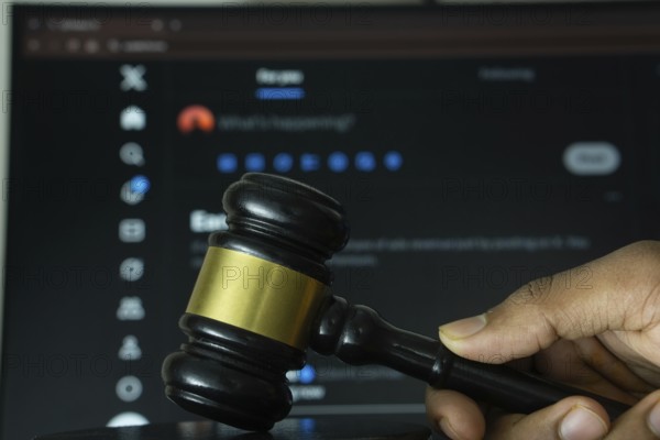 Dhaka, Bangladesh- 20 June 2025: A hand holds a gavel in front of a computer screen displaying X website